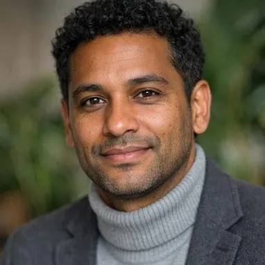 Dark-haired man in his early forties with medium brown skin, wearing a grey turtleneck